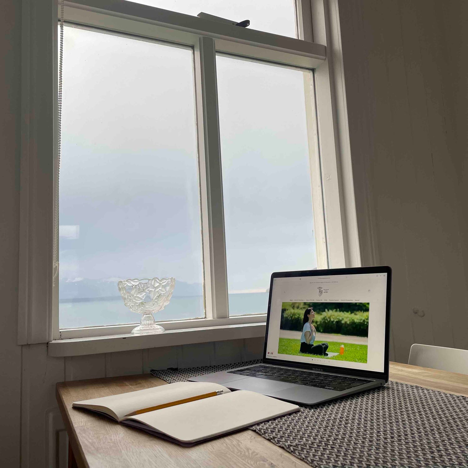 L'interno di una casa con una finestra e un bel panorama. Sul tavolo un pc che mostra l'immagine del sito web di Yoga Facciale The Face Yoga Secret