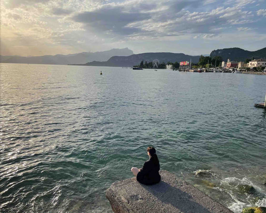 Lago, donna di spalle che guarda il lago al tramonto.