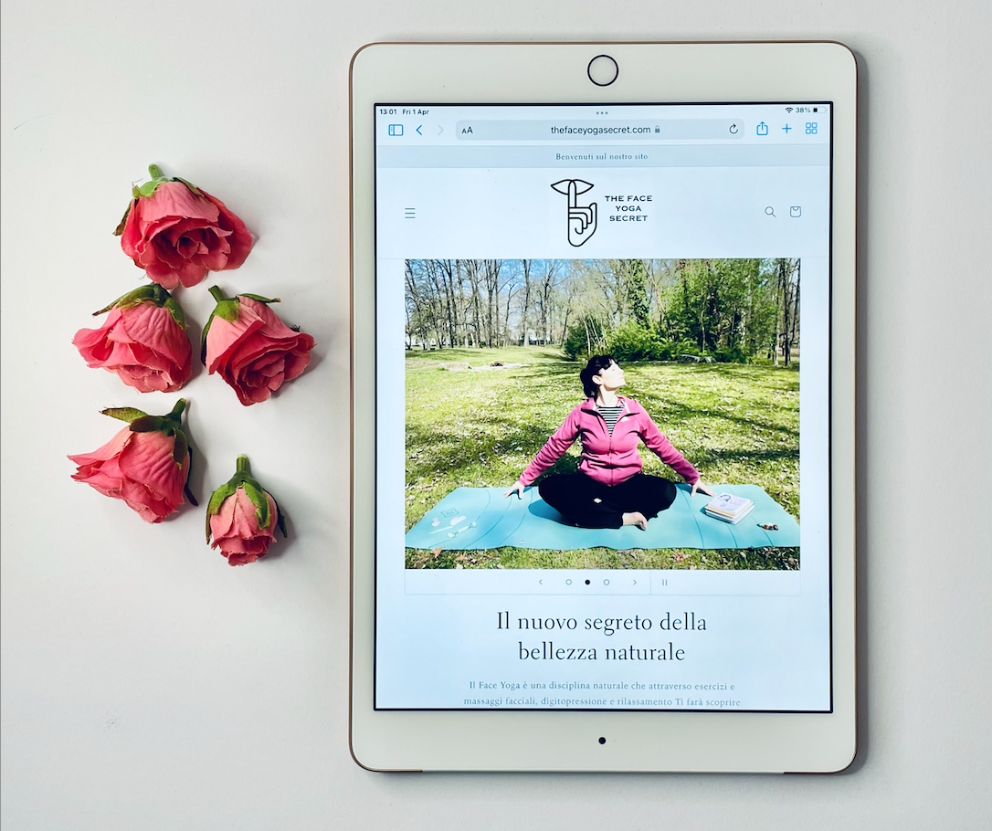 Un tablet bianco affiancato a rose rosa; l'immagine sul tablet è quella del sito web The Face Yoga Secret, brand che organizza corsi per insegnanti di Yoga Facciale